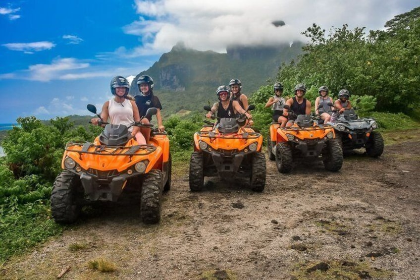 Un grupo de personas en vehículos todo terreno naranjas sobre un camino de tierra, con montañas al fondo y una masa de agua. 5