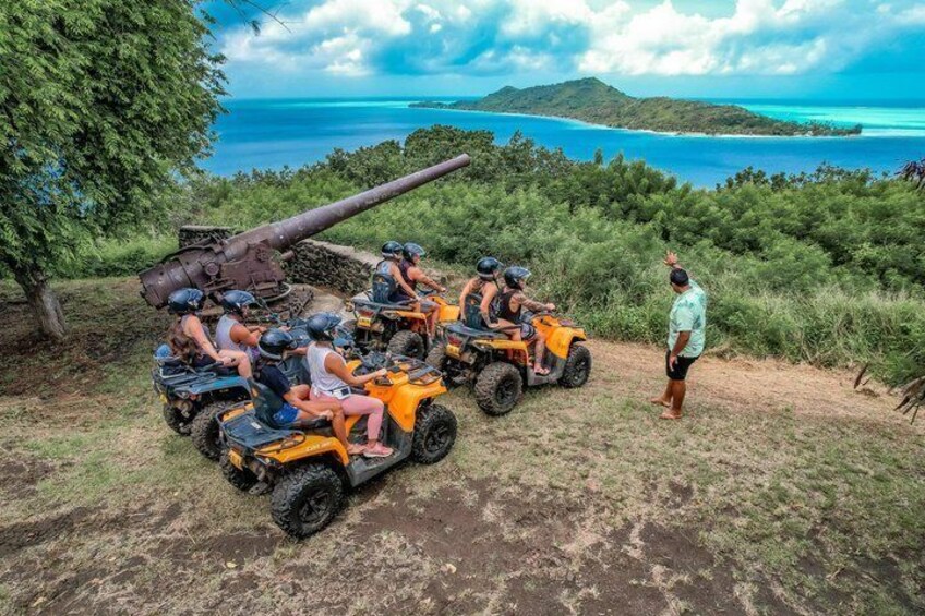 Un grupo de personas en cuatrimotos cerca de un gran cañón, con vistas a un paisaje costero de aguas azules cristalinas y colinas verdes. 2