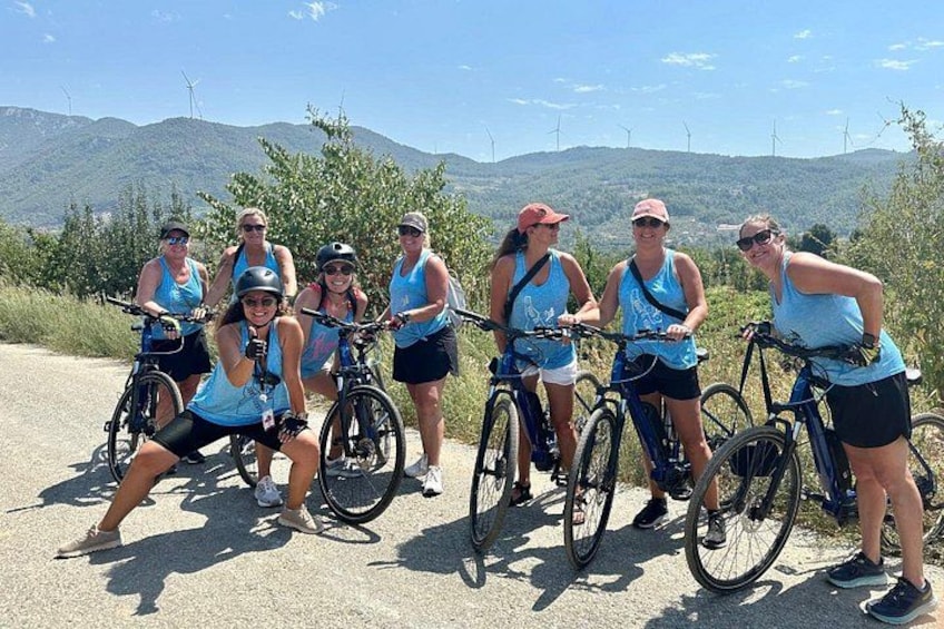 Eine Gruppe Radfahrer auf einer Straße, im Hintergrund Windkraftanlagen. 1