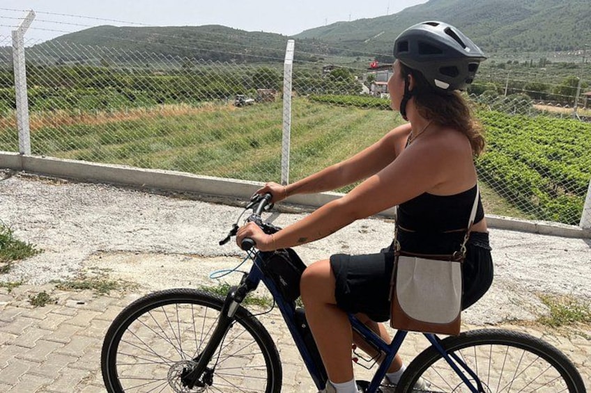 Eine Person fährt mit einem Fahrrad auf einem asphaltierten Weg, trägt einen Helm, hat eine Trinkflasche dabei und eine Tasche. 3
