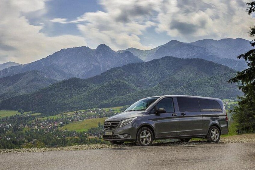 Una minivan gris estacionada en una carretera, con un paisaje montañoso al fondo. 2