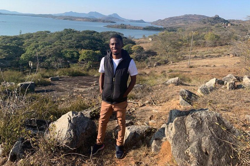 A person standing on a rocky outcrop with a view of a body of water and hills in the distance. 4