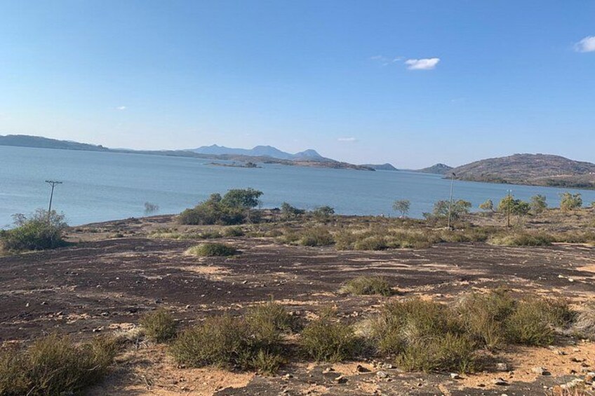 A dry, barren landscape with sparse vegetation and a large body of water in the background. 5