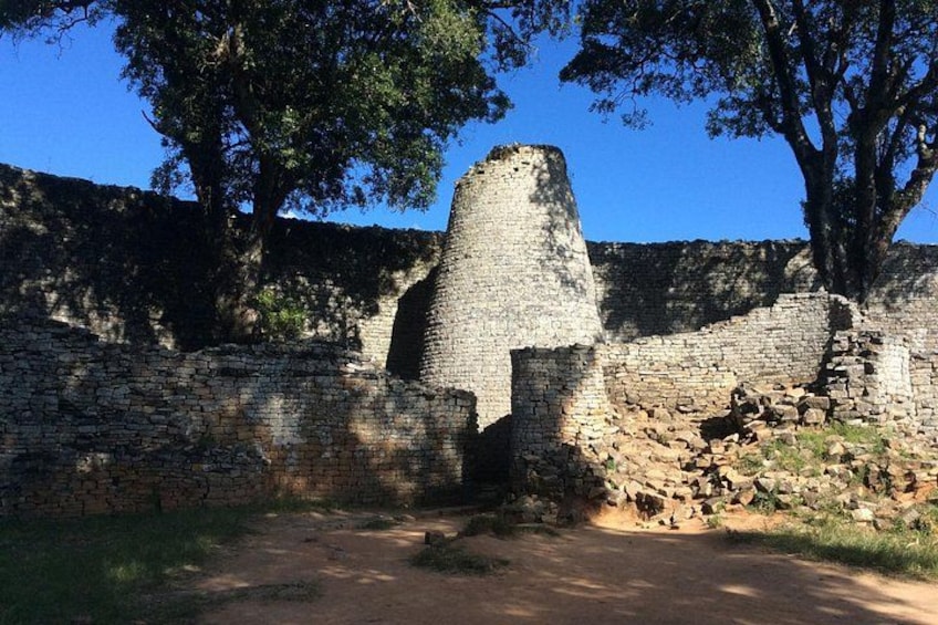 Ancient stone ruins with a prominent tower, surrounded by trees and a clear sky. 1