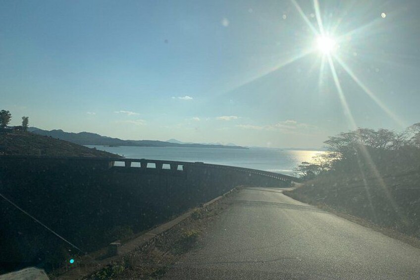 A coastal road with a guardrail, a clear sky, and the sun shining. 2