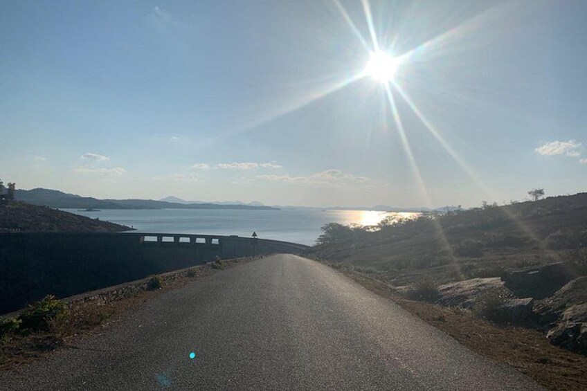 A road leading to a bridge over a body of water with a clear sky and sun. 3