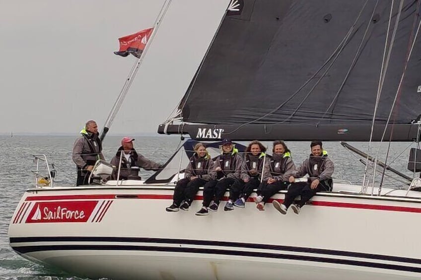 A sailboat with six people on deck, a red flag, and the word "MAST" on the sail. 2