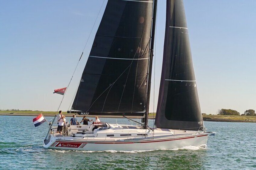 A sailboat with two sails, a Dutch flag, and a flag with a red, white, and blue design. 5