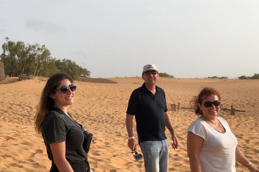 Three people standing on a sandy beach with sparse vegetation in the background. 1