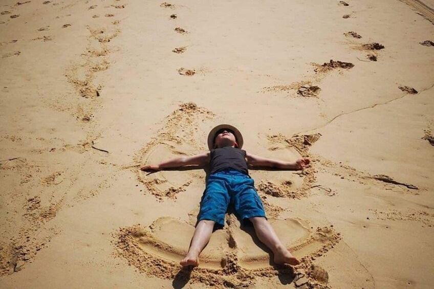 A person lying on a sandy beach with footprints around them. 2