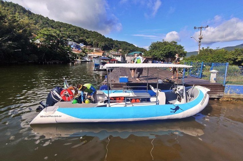 A blue and white boat docked at a pier with people on board and a forested hillside in the background. 5