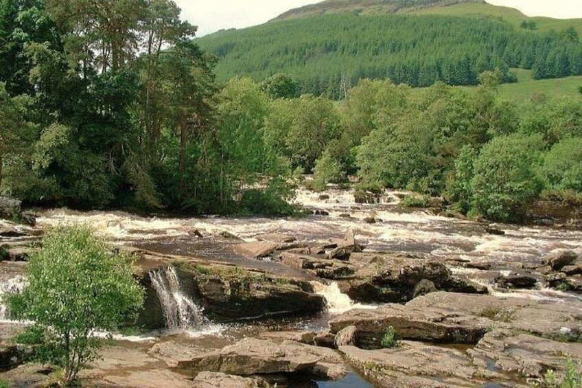 Un río que fluye sobre rocas, rodeado de un bosque denso y colinas. 5