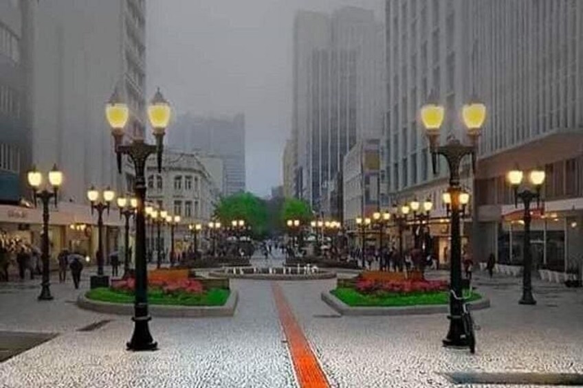 Una plaza urbana con farolas, una fuente y edificios al fondo. 3