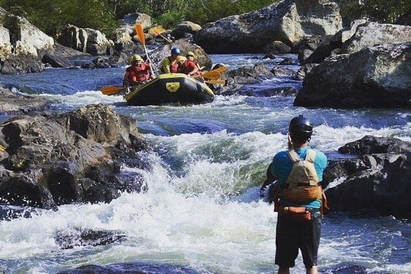 A river with rapids, a raft with people, and a person standing on the rocks. 5