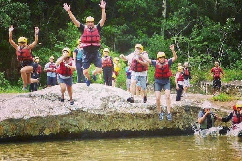 A group of people jumping off a rock into a river. 2