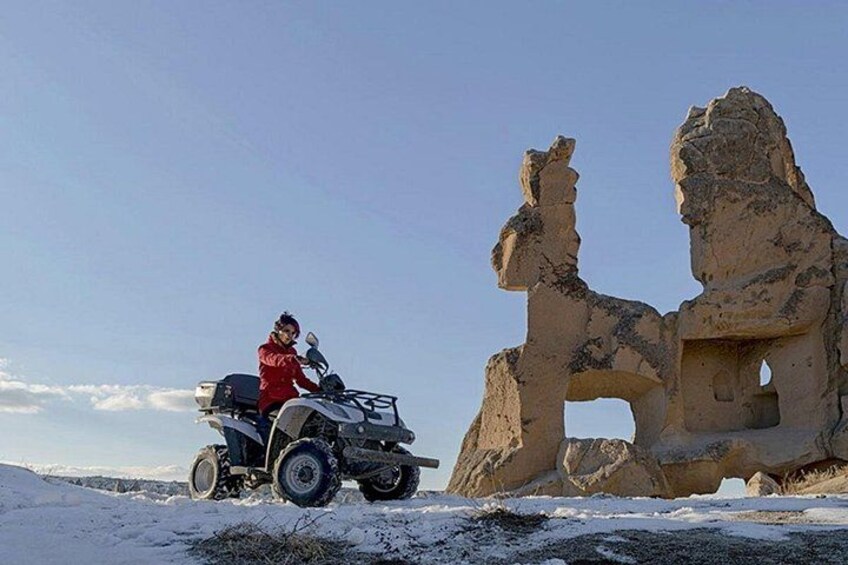 A person on a quad bike in a snowy landscape with a large rock formation. 5