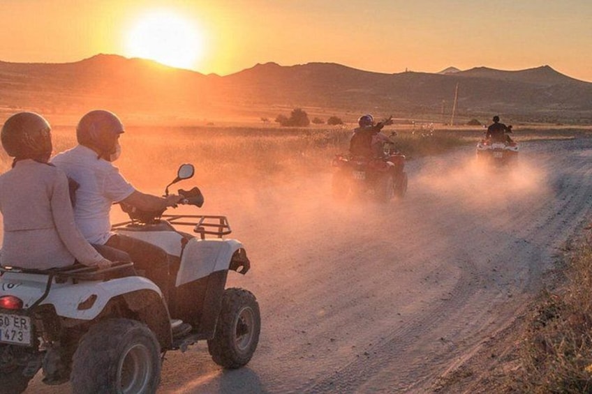 Two people on an ATV on a dirt road with a sunset in the background. 1