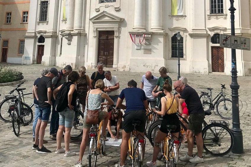 Un groupe de personnes s’est rassemblé autour de vélos devant un bâtiment historique, caractérisé par ses colonnes et sa grande porte. 3