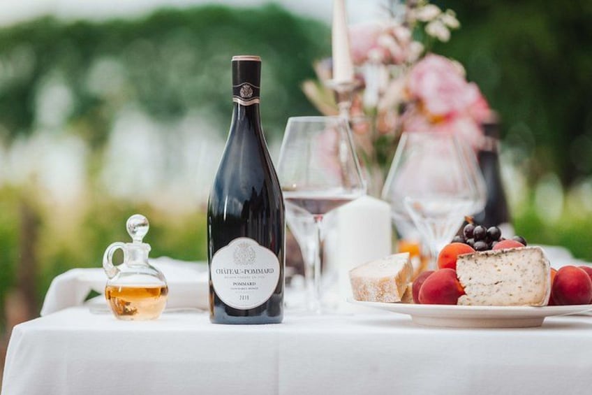 A bottle of wine, glasses, cheese, and fruit on a table outdoors. 1