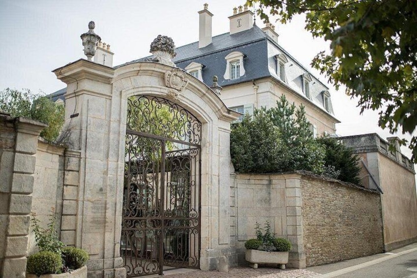 A large stone building with a wrought iron gate, surrounded by a stone wall and greenery. 3