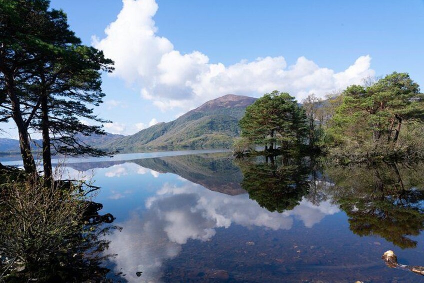 A calm lake with clear reflections, surrounded by trees and mountains. 2