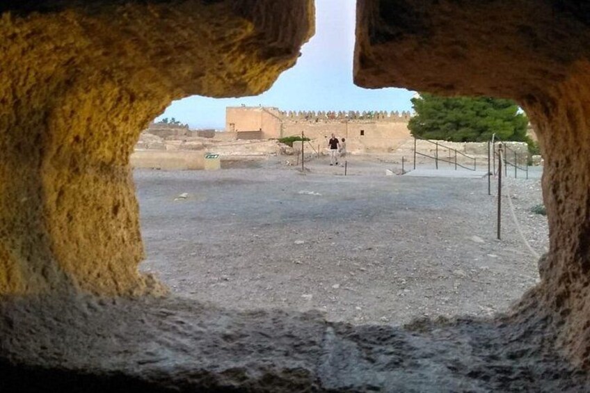 Entrada rocosa a una cueva, con vista a una zona pavimentada y un edificio distante. 5