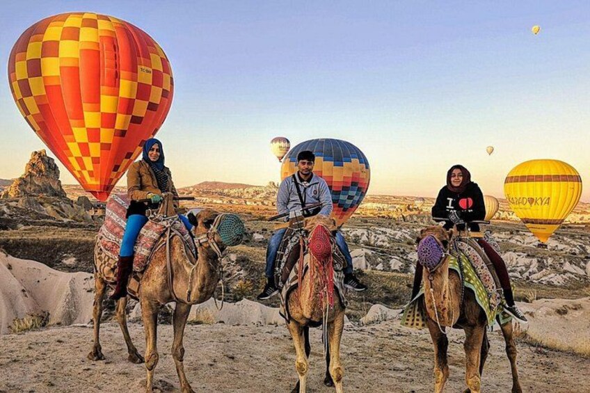 People riding camels with hot air balloons in a desert landscape. 1