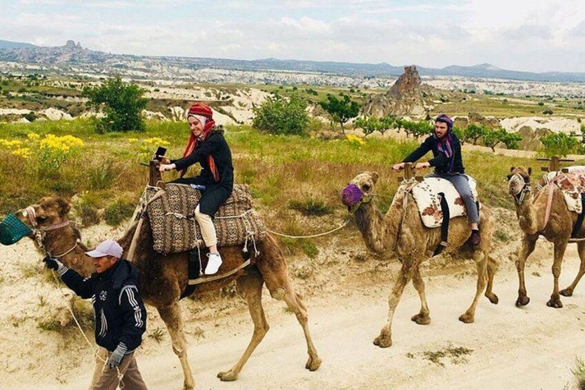 A person riding a camel, another person leading the camel, and a third person riding a camel in a desert landscape with mountains in the background. 4
