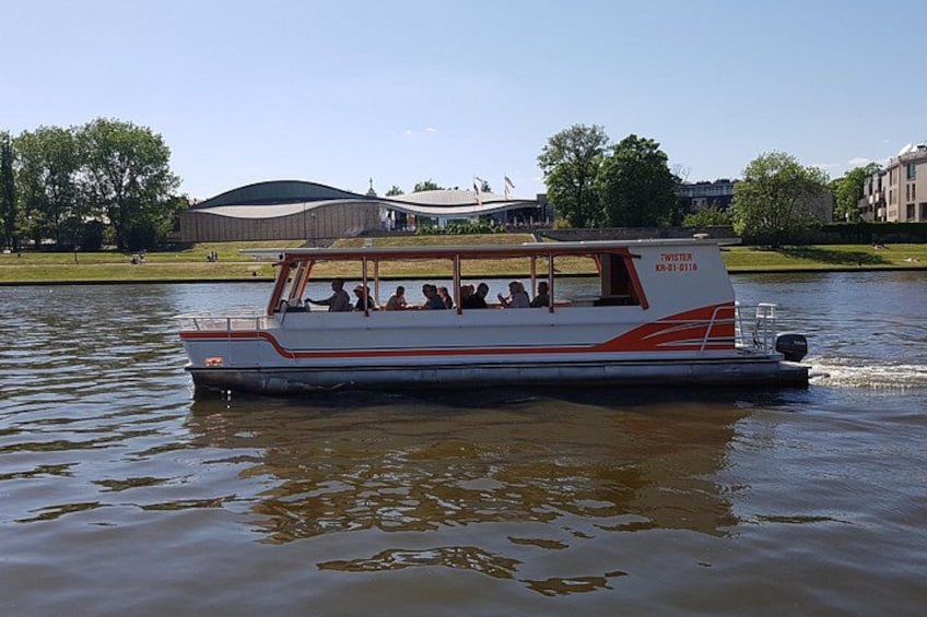 A white boat with red stripes and the name 'TWISTER' on the side, moving on a body of water with a park and buildings in the background. 4
