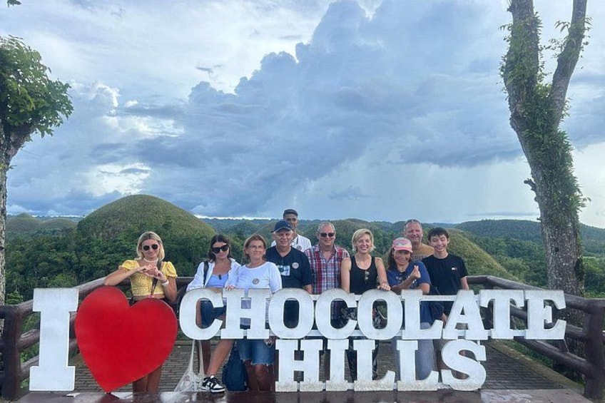 A group of people posing in front of a sign that reads 'I LOVE CHOCOLATE HILLS'. 5