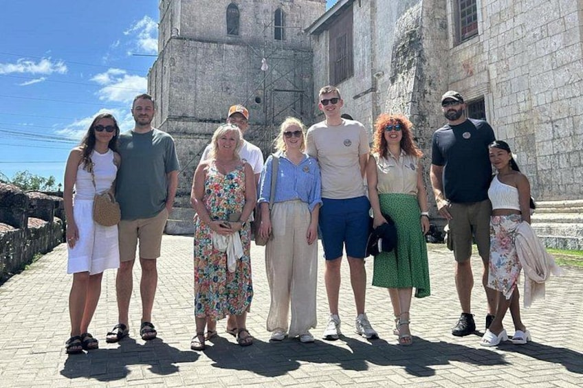 A group of people standing in front of a historic stone building with a bell tower. 3