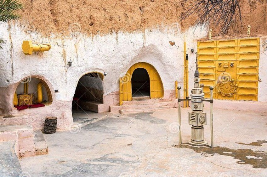 A desert landscape with a yellow gate, arched doorways, and a water spout. 4