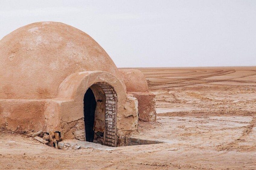 A desert landscape with a large, dome-shaped structure featuring an arched doorway. 2