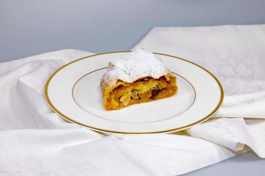 Una porción de tarta de manzana sobre un plato blanco con borde dorado, espolvoreada con azúcar glas. 1