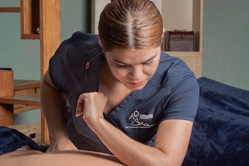 A person in a dark blue uniform with a logo, lying on a bed with a blue blanket. 4