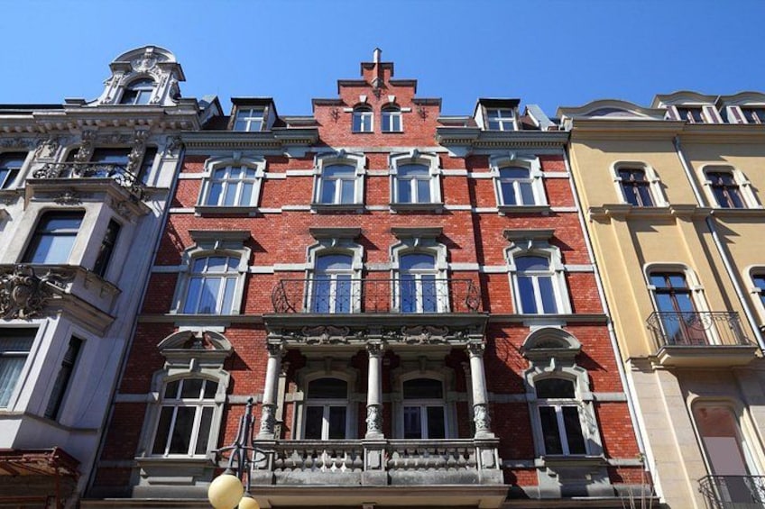 A multi-story building with red brick facade, ornate windows, and a balcony with a balustrade. 3