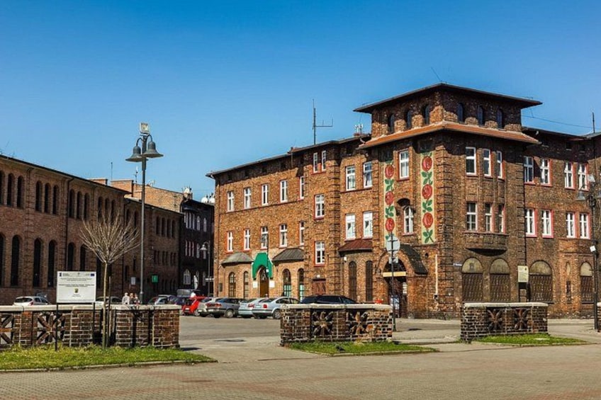 A historic brick building with arched windows and a green awning, surrounded by a paved area with a street lamp and a sign. 2