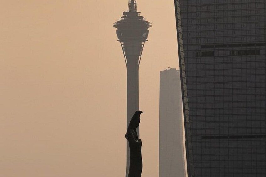 A silhouette of a person against a hazy sky, with a tall tower and a modern building in the background. 1