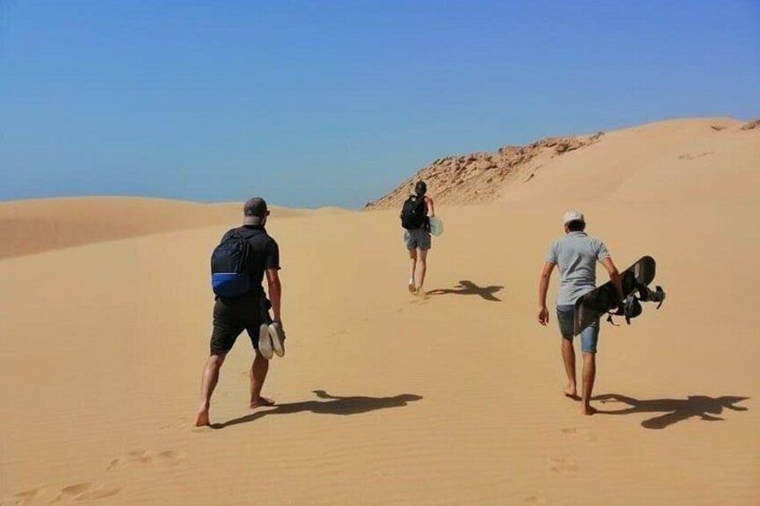 Drie mensen lopen over een zandduin, met een heldere lucht. 2