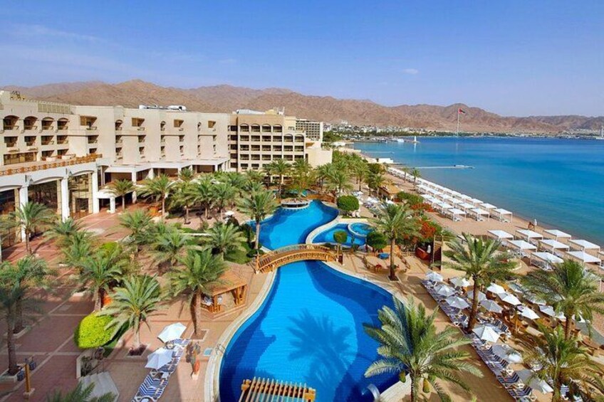 A resort with a large swimming pool, palm trees, and a beach. 3