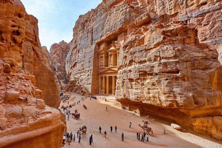A rock-cut architectural structure in a canyon with visitors. 3