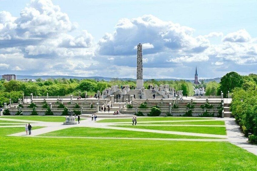 A park with a tall monument, pathways, and a distant church. 2