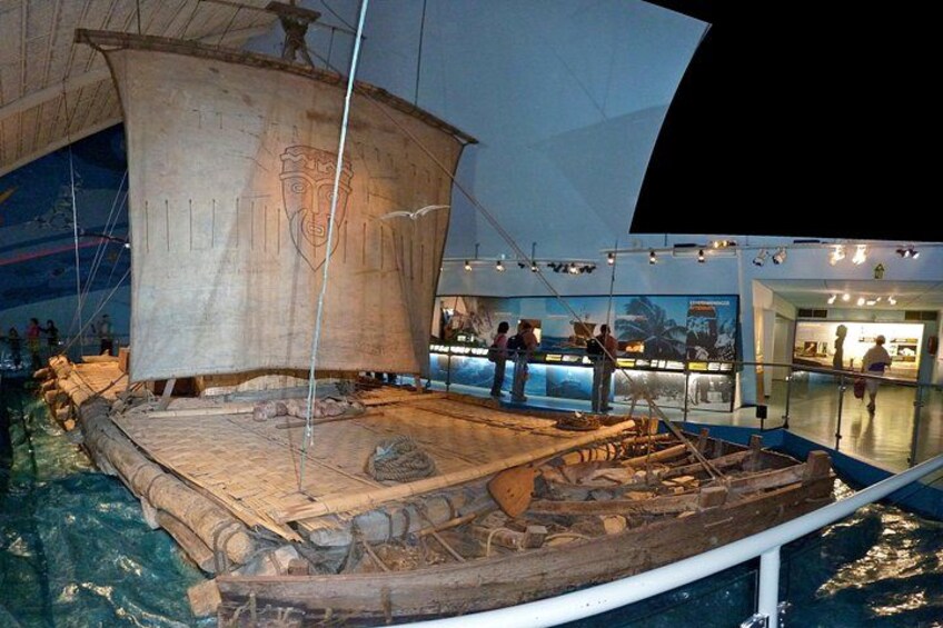 A large wooden ship model displayed indoors with a sail, surrounded by visitors. 4