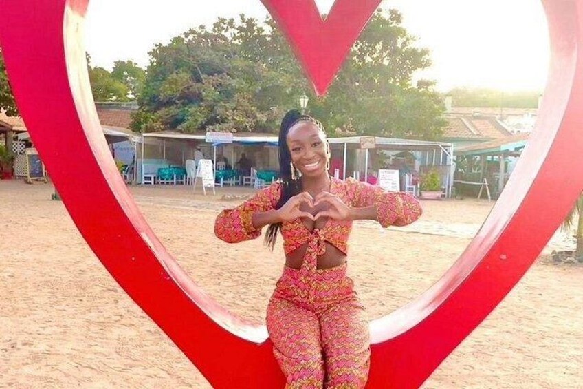 Una persona con ropa estampada posa frente a una gran estructura roja en forma de corazón. 1