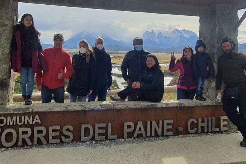 Un groupe de personnes se tient sur une plateforme d’observation, devant une pancarte sur laquelle on peut lire : « COMUNA ORRES DEL PAINE – CHILI ». 2
