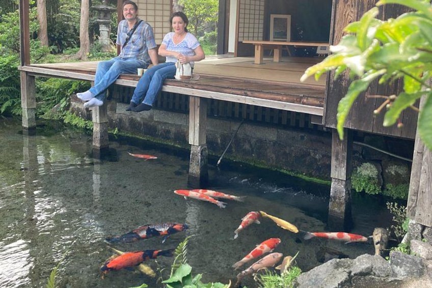 Two people sitting on a wooden deck by a pond with koi fish. 5