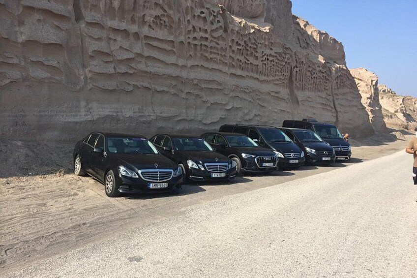A row of black cars parked on a road with a large rock formation in the background. 4
