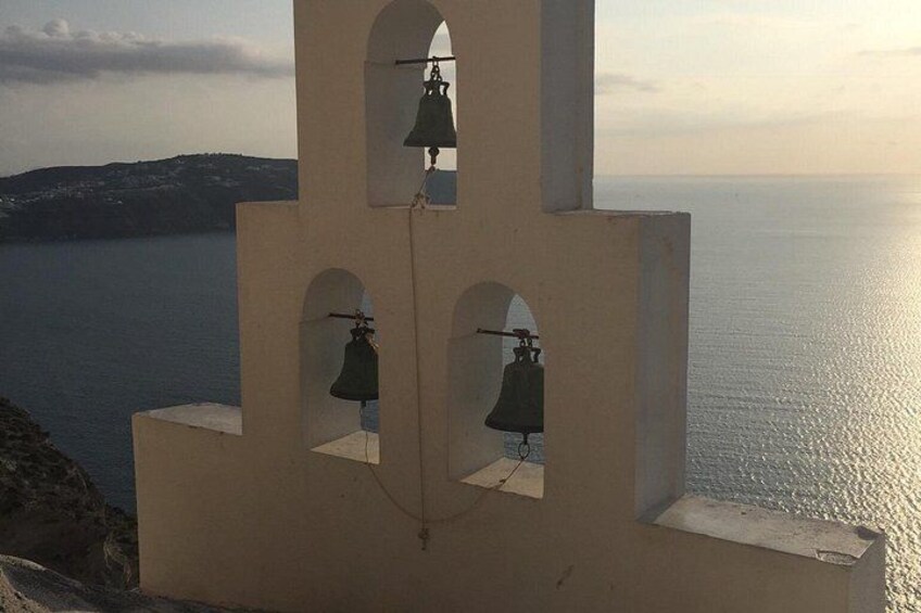 A bell tower with three bells, overlooking a calm sea and distant land. 1