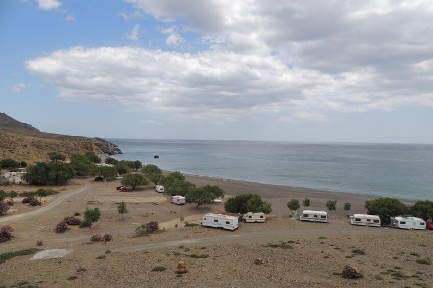 A coastal campsite with RVs and tents, a beach, and a mountainous backdrop. 2