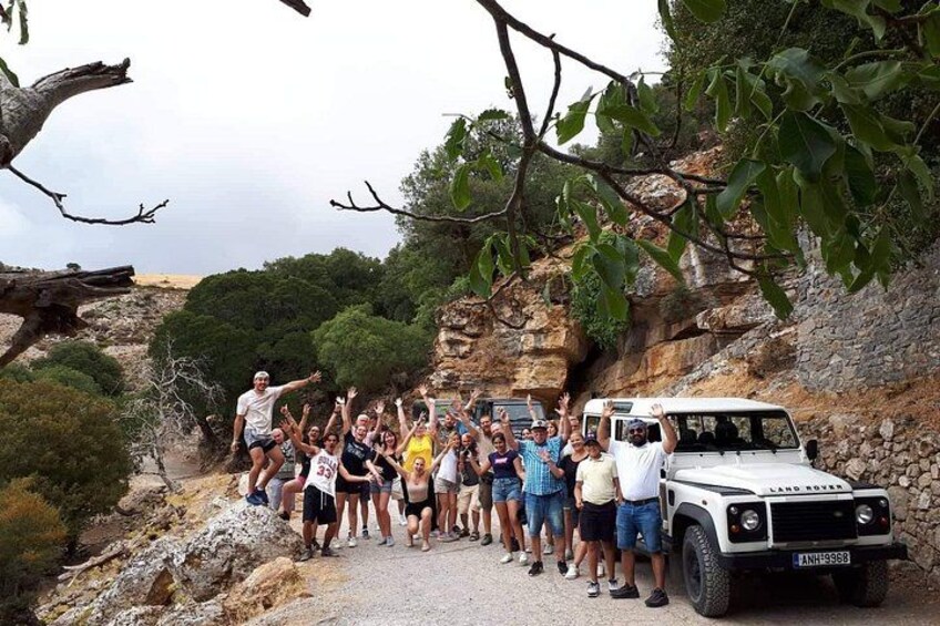A group of people posing with a Land Rover on a rocky path surrounded by trees. 1